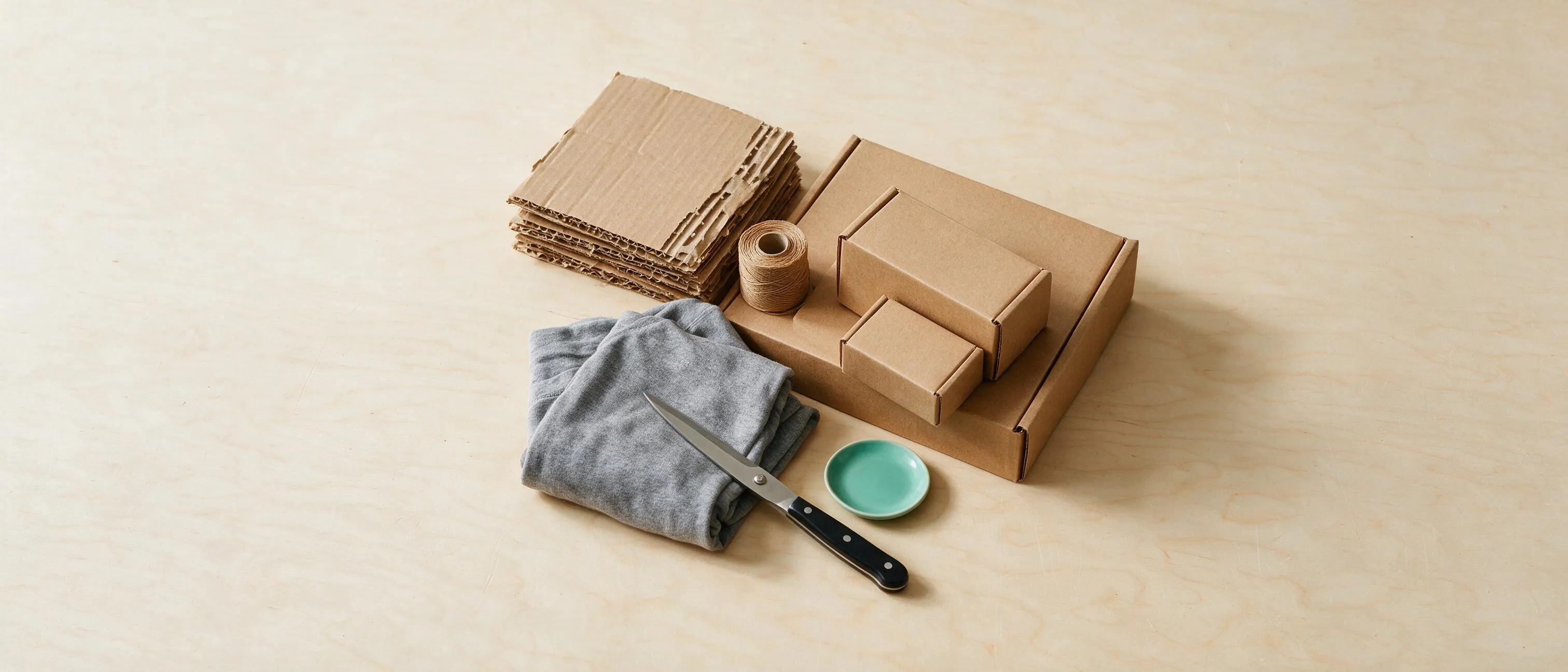 Gerecycled golfkarton, papieren touw, kraft mailerdozen op maat en een opgevouwen kledingstuk op een lichte werktafel